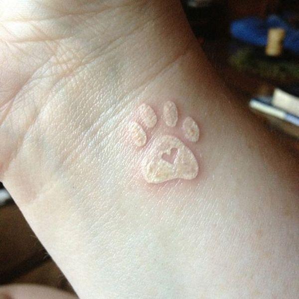 Weißes Tattoo mit Pfotenabdruck am Handgelenk
