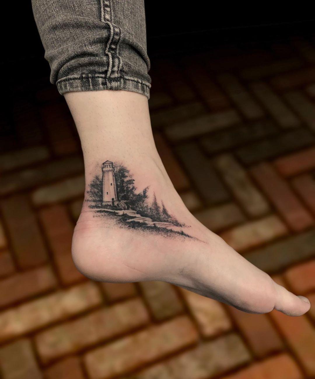 Schwarzweißes Knöchel Tattoo mit kleinem Leuchtturm und Wald