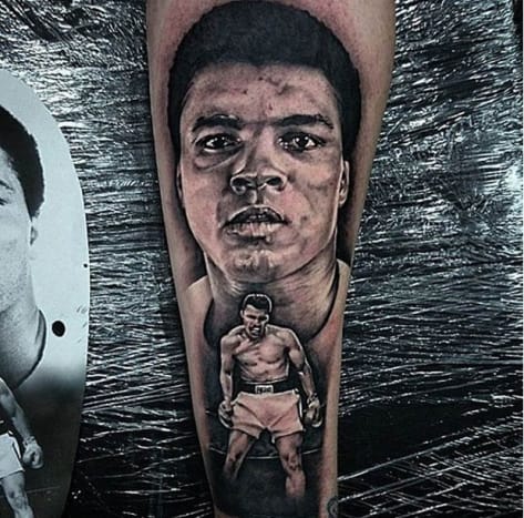 Ein weiteres beeindruckendes Porträt von Muhammad Ali. Dieses Armtattoo zeigt eine große Nahaufnahme des Boxers im Hintergrund und eine kleinere Version von Ali in demselben ikonischen Sonny Liston-Kampf im Vordergrund. Das schwarz-weiße Muhammad-Ali-Tattoo wurde von Kit Maxwell, Tätowierer bei Forbidden Ink in Großbritannien, gemacht und trug einfach die Überschrift „RIP-Legende!“