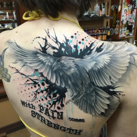 Raven and Quote Back Tattoo Toto tetování na zádech této ženy bylo napuštěno Joshem A. z Clever Rebel Tattoo ve státě Washington a je na něm černobílý obraz havrana v letu s citátem „S bolestí přichází síla“, provedeno odvážným černým psacím strojem písmo. Pozadí tetování je potřísněno černým inkoustem se symetrickými černými a aqua modrými kruhy, které se rozprostírají k jejímu pravému rameni a levé spodní části zad.