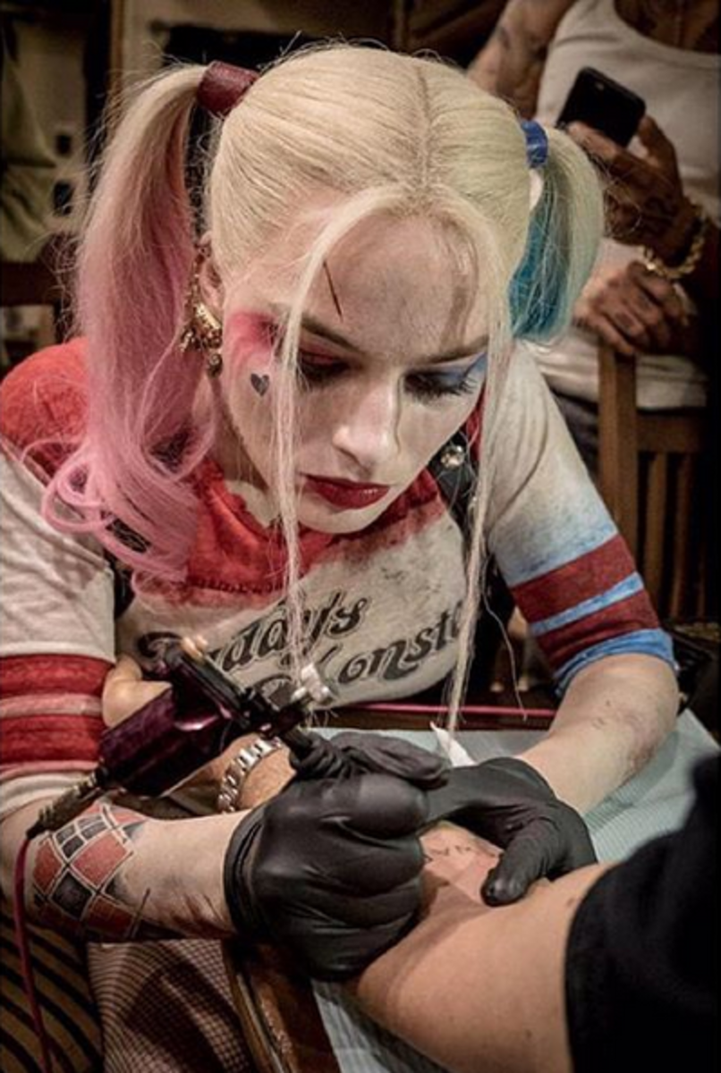 Margot Robbie (immer noch im Kostüm als eingefärbte Harley Quinn) tätowiert einen ihrer Mitstars.