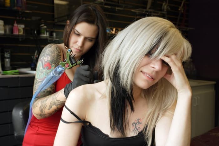 Samice tetování, která ve třiceti letech nanáší své řemeslo na záda a paži ženy. (Vydání nemovitosti pro tetování je přiloženo)