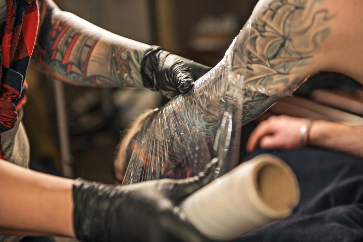 tetování-umělec-obal-klient-s-paže-v-plastu-přilnavý film-k podpoře-tetování-hojení