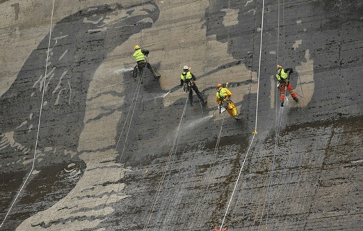 Umělci/pracovníci zmenšují zeď přehrady, aby se dostali zblízka a osobně.