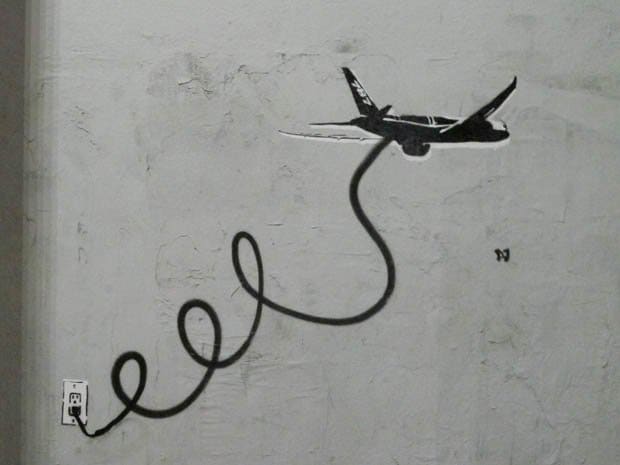 Fly By Wire - Streetart-Künstler in Los Angeles - PLASTIC JESUS ​​nimmt Boeings Probleme mit dem Flaggschiff 787 Dreamliner unter die Lupe. Die Schablonen-Graffiti, die in Los Angeles entdeckt wurden' Melrose distict zeigt das Flugzeug, das über ein Kabel an eine Steckdose angeschlossen ist, um elektrische Probleme zu lösen, die das Flugzeug geerdet haben.