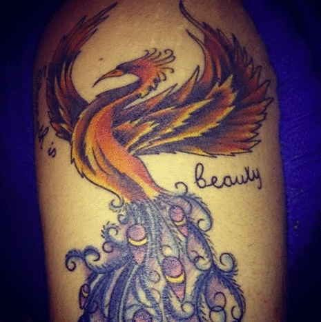 Hier ist ihr Phoenix / Peacock-Tattoo auf ihrem linken Oberarm. Sie kombinierte sie, um der Welt und sich selbst ihre Stärke und Eleganz zu zeigen. Neben dem Vogel steht: