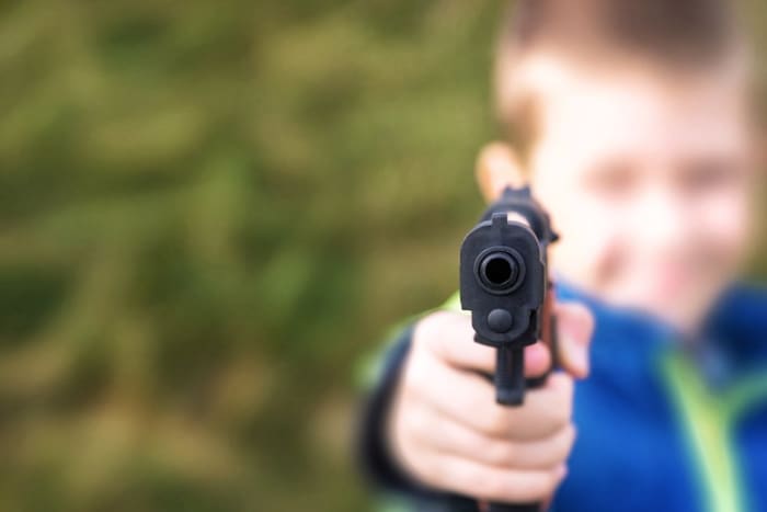 kleiner Junge, der mit der Waffe auf die Kamera zeigt
