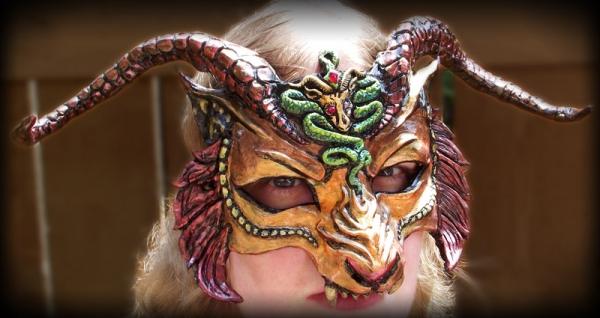 CHIMERA-MASKE Eine dem mythischen Monster Chimera nachempfundene Maske in sattem Gold, Orange und Rot. Traditionell hatte die Chimäre einen Löwenkörper, einen Löwen- und Ziegenkopf und einen Schlangenschwanz. Der Künstler verlieh der Maske den Kopf eines gehörnten Löwen mit einer sich nach unten windenden Schlange und einem Ziegenemblem auf der Stirn. Ziege und Schlange haben leuchtend rote Augen und in die Stirn der Schlange ist ein tränenroter Edelstein eingefasst. Die Maske ist vollständig von Hand geformt und bemalt und hat auf der Rückseite einen Künstlerstempel mit dem Entstehungsdatum. Die Maske ist leicht und die Hörner sind etwas flexibel, um das Risiko von Beschädigungen zu verringern. Mit Hörnern ist die Markierung 14