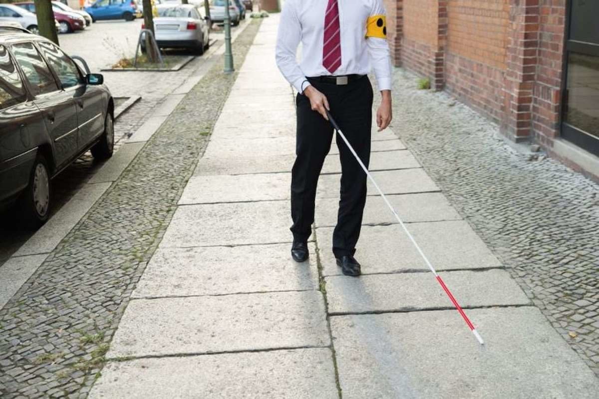 Popis fotografie: Muž v kravatách a kalhotách chodí s holí po sousedním chodníku
