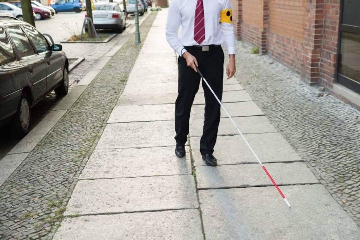 Fotobeschreibung: Mann in Krawatte und Anzughose, der mit Gehstock über den Bürgersteig in der Nachbarschaft geht