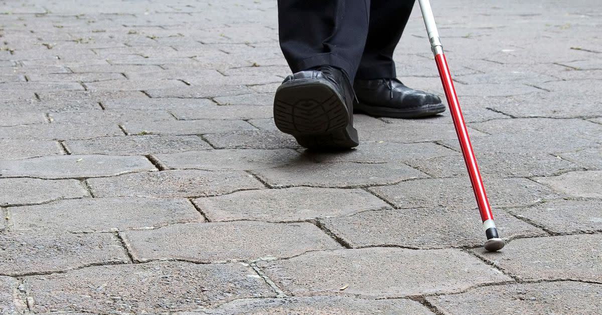 Popis fotografie: Detailní záběr na mužské nohy s holí na dlážděném chodníku